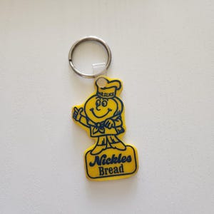 May include: Yellow keychain featuring a cartoon chef with the text "Mr. Slice" and "Nickles Bread" in blue. The chef is giving a thumbs up. The keychain has a silver ring.