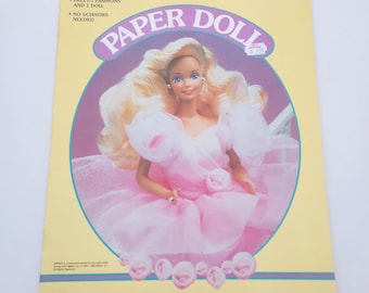 May include: A vintage Barbie paper doll book with a yellow cover. The cover features a Barbie doll in a pink dress, with the words "Barbie Paper Doll" in a purple circle. The book includes precut fashions and a doll.