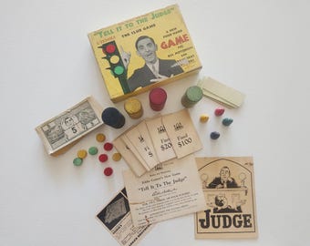 May include: A vintage board game, "Tell It To The Judge", with a box showing a man and a traffic light. The set includes game cards, wooden tokens, play money, and a "Judge" card. A classic game for motorists.