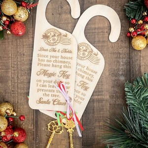 May include: Two wooden door hangers with a gold key and a red, white, and green ribbon. The hangers are decorated with a North Pole Express stamp and the text "Dear Nia & Nahla, Since your house has no chimney, please hang this Magic Key on your door so I can leave your presents under the tree. Santa Claus".