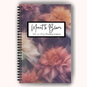 May include: A spiral-bound journal with a floral design in shades of pink, peach, and purple. The cover features the text "Meant to Bloom" above "The 90 Day Planning Journal" in a black rectangle.