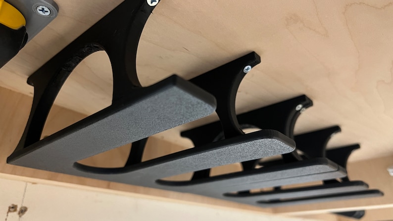 May include: Three black plastic wall-mounted storage shelves with a textured finish. The shelves are mounted under a wooden surface.