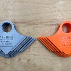 May include: Two sets of 3D-printed tools. One set is grey and labeled "1/4 Inch ARTISAN MADE." The other set is orange and labeled "1/2 Inch ARTISAN MADE." Each tool has a circular handle and a notched edge.