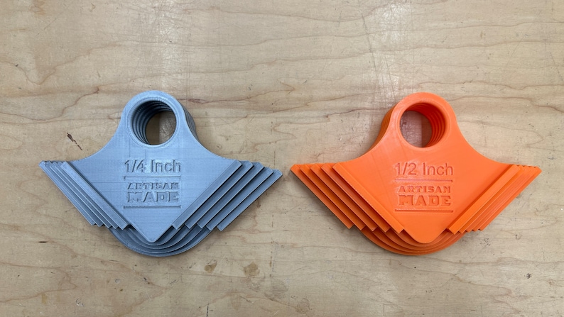 May include: Two sets of 3D-printed tools. One set is grey and labeled "1/4 Inch ARTISAN MADE." The other set is orange and labeled "1/2 Inch ARTISAN MADE." Each tool has a circular handle and a notched edge.