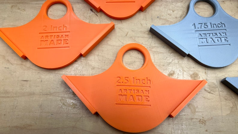 May include: Several orange and one grey artisan-made tools with a handle and angled edge. The tools are labelled with measurements: 2 inches, 2.5 inches, and 1.75 inches. The text "ARTISAN MADE" is also printed on each tool.