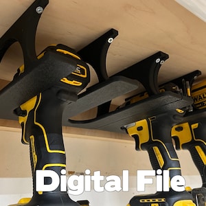 Puede incluir: Un soporte de pared impreso en 3D para guardar herramientas eléctricas. El soporte es negro y tiene dos ranuras para sujetar taladros. Los taladros son amarillos y negros y están colgados del soporte. El texto "Digital File" es visible en la imagen.