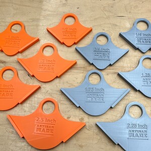 May include: A selection of orange and grey artisan-made measuring tools. The tools are labelled with inch measurements ranging from 0.64 cm to 6.35 cm. Each tool has a handle and the text "ARTISAN MADE".
