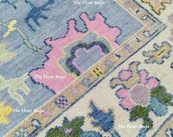 Puede incluir: Primer plano de una alfombra hecha a mano con un campo central azul claro. La alfombra presenta patrones florales y geométricos en colores rosa, verde y crema. El texto "The Floor Rugs" es visible en la imagen.