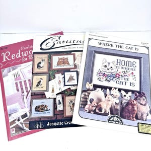 May include: Three books with cat-themed designs. One book is titled "Redwood for B" with a crib illustration. Another is "Cattitude" with various cat images. The third book is "Where the Cat Is".