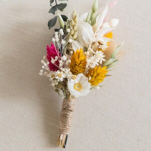 Könnte beinhalten: Ein kleiner Strauß getrockneter Blumen, die mit einer Schnur zusammengebunden sind. Der Strauß enthält weiße, gelbe, rosa und grüne Blumen.