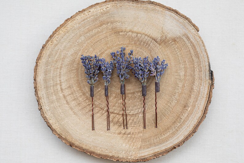 Pode incluir: Cinco grampos de cabelo de lavanda com hastes de arame marrom em uma superf&iacute;cie de madeira.
