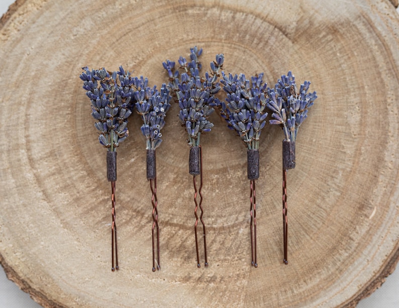 Pode incluir: Conjunto de seis grampos de cabelo de lavanda com hastes de fio de cobre. A lavanda &eacute; seca e de cor roxa. Os grampos est&atilde;o dispostos sobre uma superf&iacute;cie de madeira.