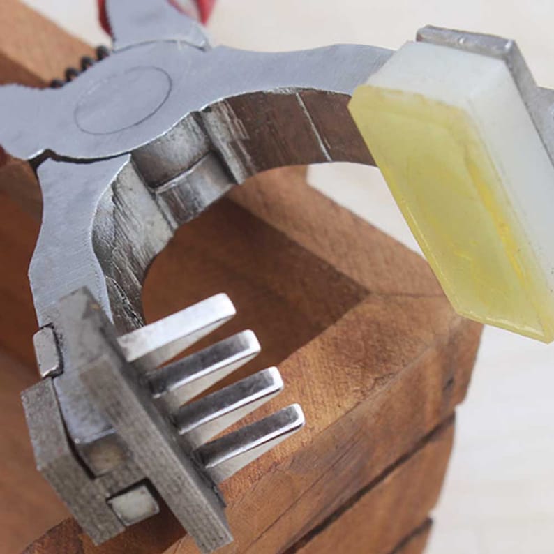 May include: A metal tool with a handle and a set of prongs. The tool is used to punch holes in leather or other materials. The tool is resting on a wooden surface.