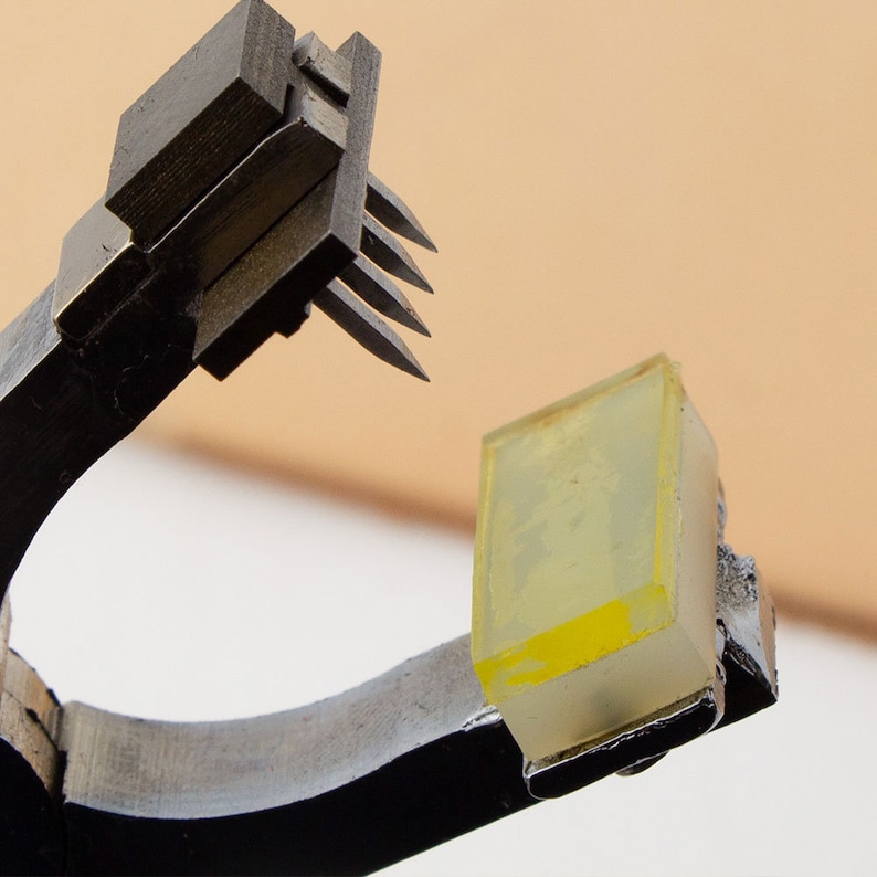 May include: A black metal tool with a set of sharp metal prongs, holding a clear yellow rectangular object.