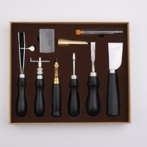 May include: A set of leather working tools in a brown box. The tools include a stitching awl, a stitching groover, a stitching chisel, a leather skiver, a leather punch, a leather edge beveler, and a leather burnisher.