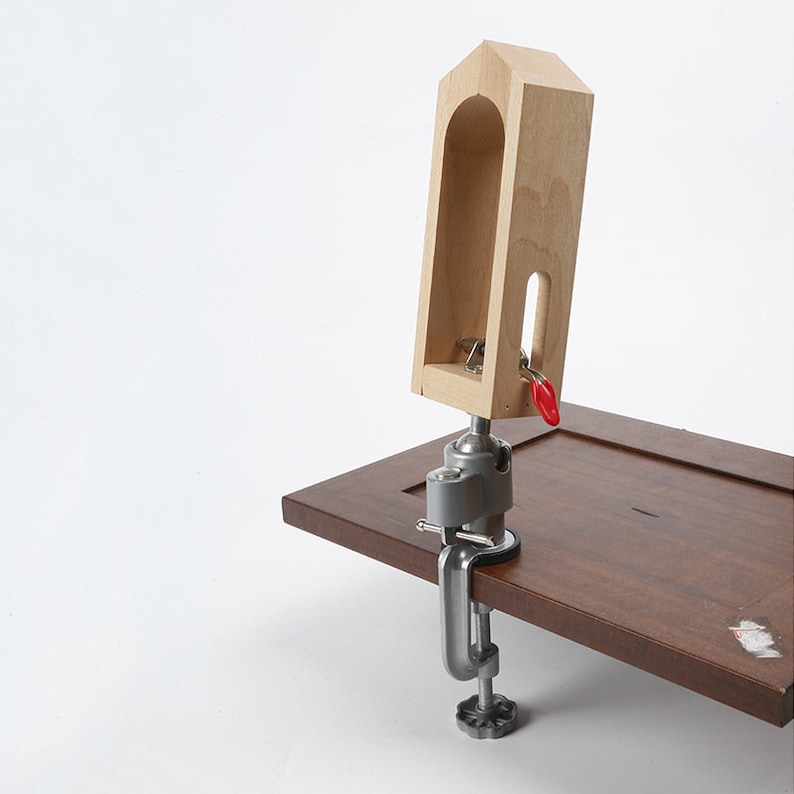 May include: A wooden clamp with a red handle, attached to a silver clamp, is mounted on a brown wooden surface.