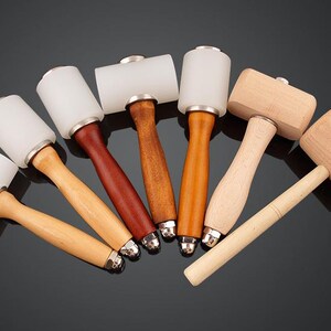 May include: A set of seven leather working mallets with wooden handles. The mallets have white rubber heads and wooden heads.