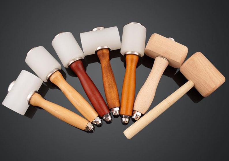 May include: A set of seven leather working mallets with wooden handles. The mallets have white rubber heads and wooden heads.