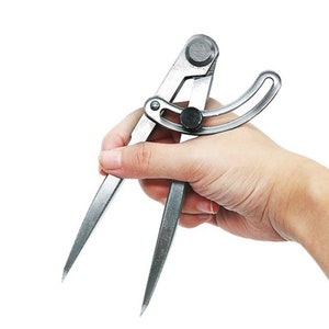 May include: A silver compass with a black knob and a curved handle. The compass is used for drawing circles and arcs.