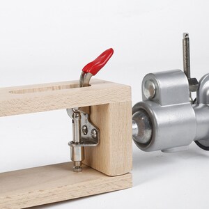 May include: A wooden leather working clamp with a red lever and a silver metal clamp. The clamp is used to hold leather pieces together while stitching.