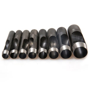 May include: A set of eight black metal hole punch tools with different sized round holes. The tools are arranged in a row from smallest to largest.