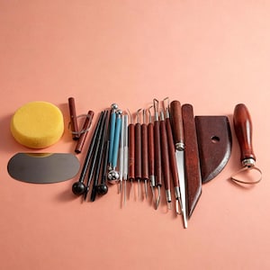 May include: A collection of pottery sculpting tools including a yellow sponge, a metal scraper, wooden-handled wire loops, ball styluses, and wooden modeling sticks. The set features various metal tips, blades, and loops for shaping clay projects.