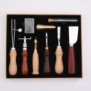 May include: A set of eight leather crafting tools in a brown box. The tools include a stitching awl, a stitching groover, a stitching chisel, a stitching pony, a leather skiver, a leather punch, a leather edge beveler, and a leather burnisher.