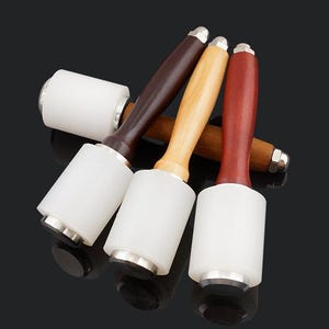 May include: Four leather working mallets with wooden handles. The mallets have white rubber heads and silver metal accents.