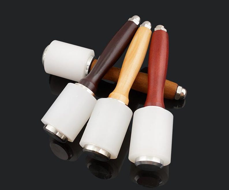 May include: Four leather working mallets with wooden handles. The mallets have white rubber heads and silver metal accents.