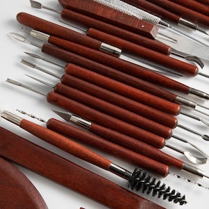 May include: A set of 20 clay sculpting tools with wooden handles and various metal tips. The tools are arranged in a row, with the handles facing the viewer. The tools are used for shaping, smoothing, and detailing clay.