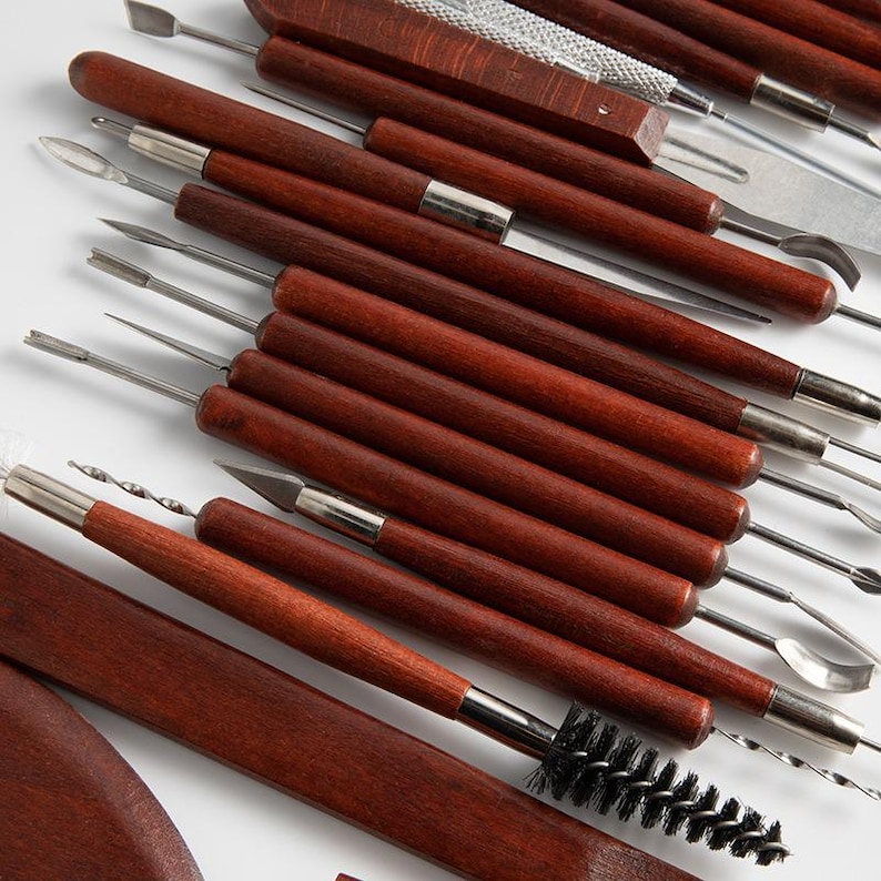 May include: A set of 20 clay sculpting tools with wooden handles and various metal tips. The tools are arranged in a row, with the handles facing the viewer. The tools are used for shaping, smoothing, and detailing clay.