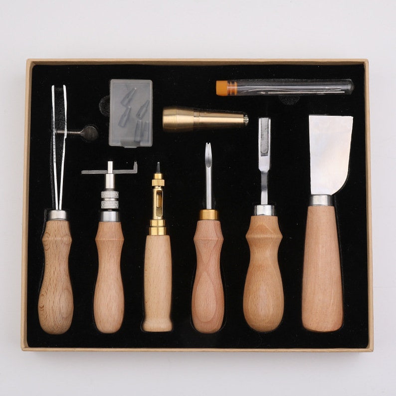May include: A set of leather working tools in a wooden box. The tools include a stitching awl, a stitching groover, a stitching punch, a stitching chisel, a stitching pony, a stitching needle, and a stitching thread. The tools are all made of metal with wooden handles.