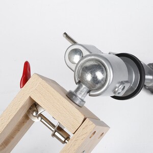 May include: A silver metal clamp with a wooden base and a red lever. The clamp is adjustable and can be used to hold objects in place.
