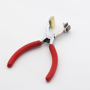 May include: A red-handled metal tool with a yellow pad and a small metal piece with teeth. The tool is used for punching holes in leather or other materials.
