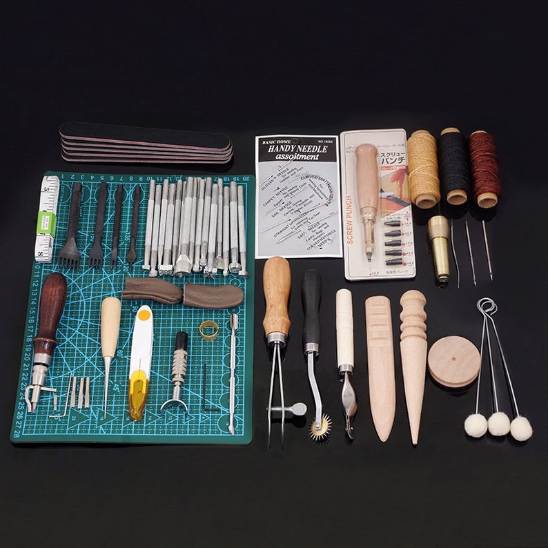 May include: A leather craft tool kit with a variety of tools, including punches, awls, needles, thread, and a stitching pony. The tools are laid out on a green cutting mat with a ruler and a black sanding block.