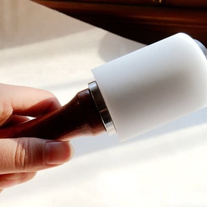 May include: A white leather mallet with a wooden handle. The mallet is used for leatherworking and crafting.