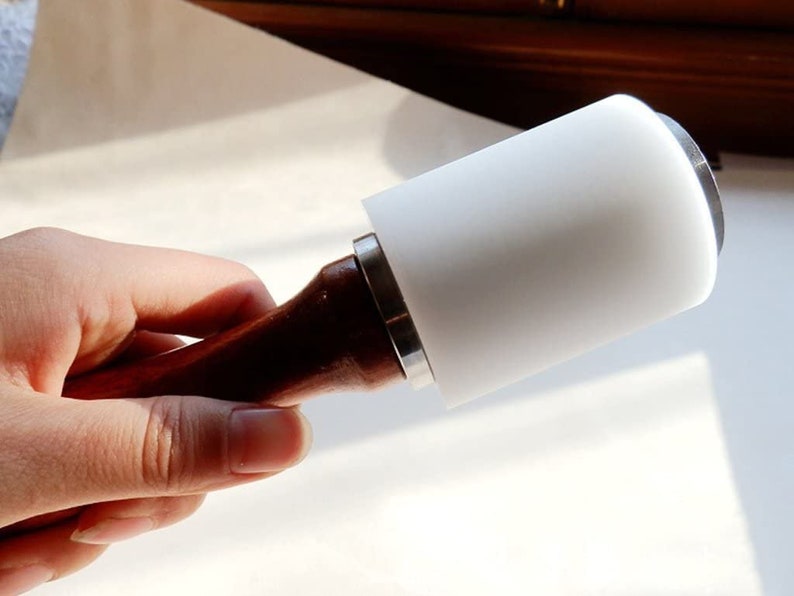 May include: A white leather mallet with a wooden handle. The mallet is used for leatherworking and crafting.