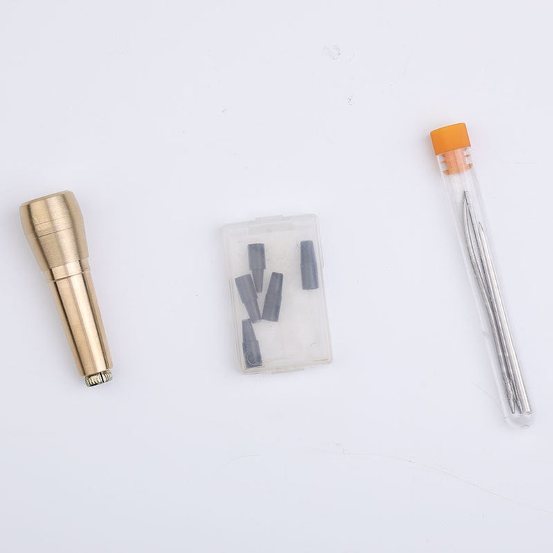 May include: A set of leather crafting tools including a brass awl, a small plastic container with several awl tips, and a clear plastic tube containing two needles.