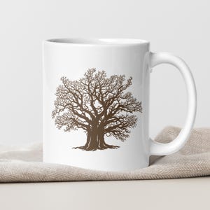 Può includere: Tazza in ceramica bianca con una silhouette marrone di un grande albero con rami intricati. La tazza ha un manico curvo e poggia su un tessuto beige. Il disegno dell'albero è centrato sulla tazza.