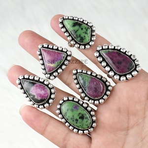 Puede incluir: Una colección de anillos de plata con diversas formas de piedras preciosas. Los anillos presentan piedras verdes y rojas, engastadas en un bisel de plata con un borde de cuentas. Las piedras tienen patrones y colores únicos.