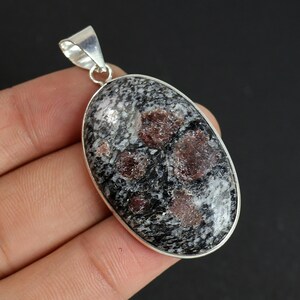 Może przedstawiać: Owalny wisiorek ze srebrnym uchwytem. Wisiorek posiada nakrapiany czarno-szary kamień z bordowymi wtrąceniami. Kamień osadzony jest w srebrnej oprawie.