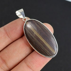 May include: Oval pendant with a polished, striped stone in shades of brown and tan, set in a silver-colored metal frame. The pendant has a loop at the top for a chain.