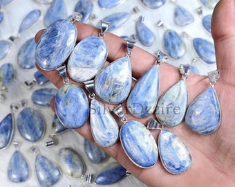 May include: A collection of blue kyanite pendants featuring polished, oval and teardrop-shaped gemstones set in silver-toned metal frames. Each pendant displays a unique, fibrous, and chatoyant texture with varying shades of light to deep blue.
