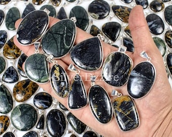 May include: A collection of polished, dark-toned gemstone pendants set in silver-coloured metal frames. The stones feature intricate, natural veining in shades of black, deep blue, and earthy gold. Each pendant includes a small metal bail for hanging.