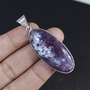 Puede incluir: Un colgante de plata con una gran piedra ovalada de color púrpura y blanco. La piedra preciosa tiene un patrón de remolino de púrpura, blanco y negro.
