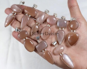 Puede incluir: Una colección de colgantes de piedras preciosas en varias formas, incluyendo ovaladas, de lágrima y rectangulares, con una fianza plateada. Los colgantes son de color melocotón y marrón claro. El texto "SilverDzzire" es visible.