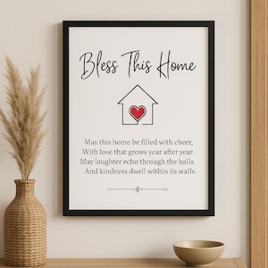 Pode incluir: Impressão emoldurada com as palavras "Bless This Home" em escrita elegante. Abaixo do texto, um ícone de casa com um coração vermelho. A impressão inclui um poema sobre casa e é exibida em uma mesa de console de madeira.
