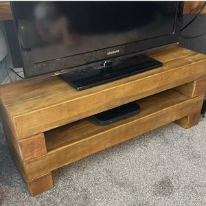 Może przedstawiać: Rusztyczny drewniany stojak na telewizor z półką, w ciemnobrązowym wykończeniu i telewizorem Samsung na górze.