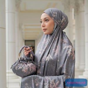 May include: A gray floral print prayer shawl with a matching handbag. The shawl is draped over the shoulders and head of a person. The text "KANAYAHIJAB" is visible in the bottom right corner of the image.