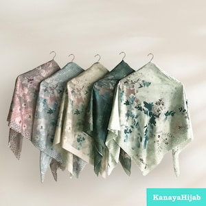 May include: Five floral patterned scarves in shades of green, beige, and pink hanging on hangers. The scarves have a delicate floral print and a subtle shimmer.